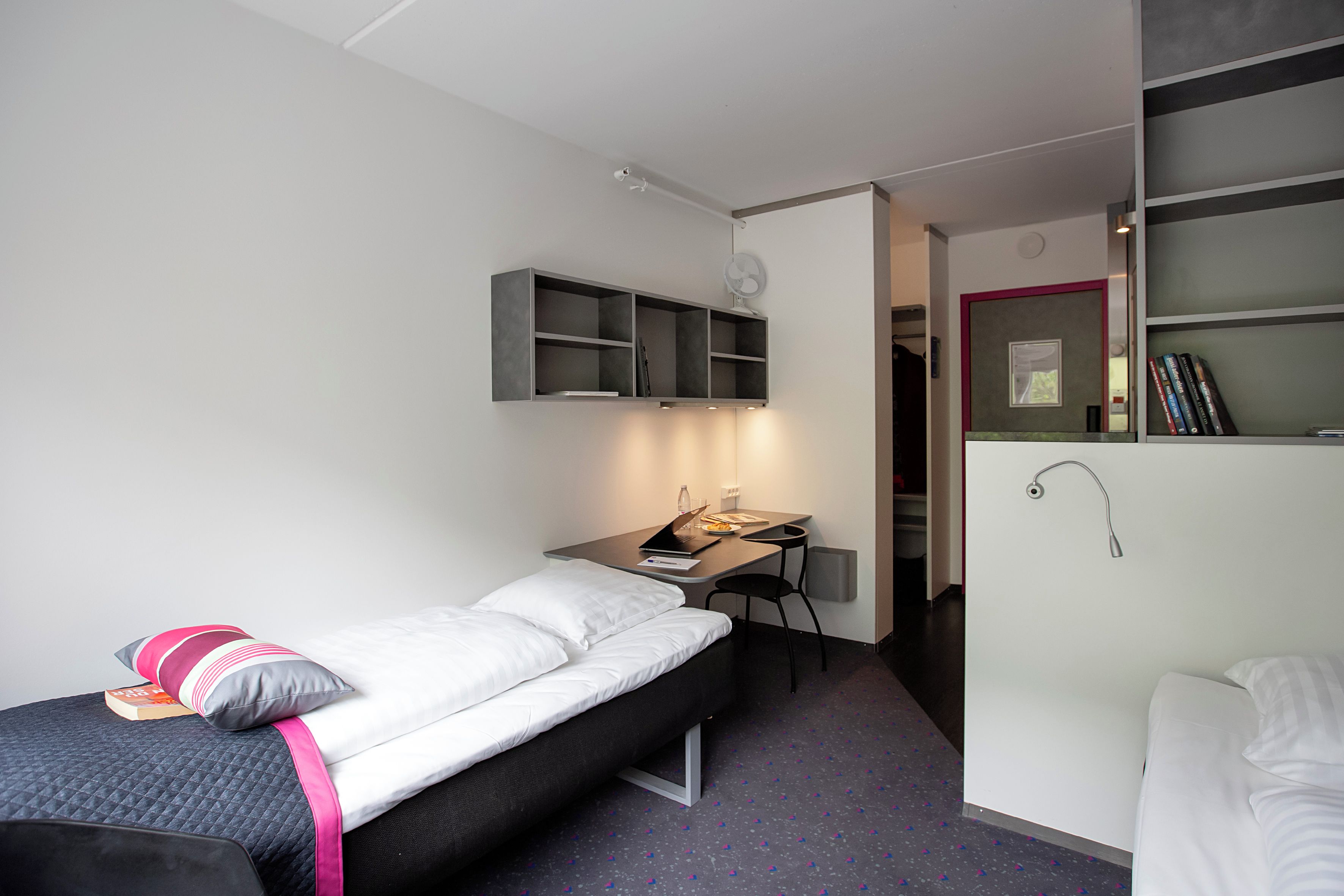 A compact hotel room with a single bed, a desk, and a small seating area.