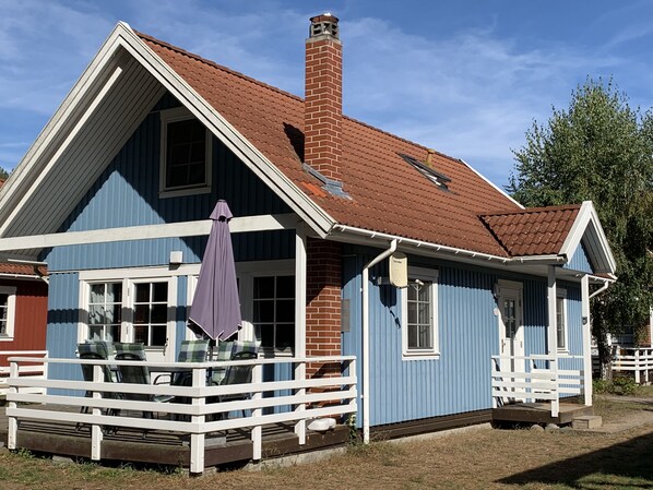 Une maison à deux étages avec un porche, une cheminée et un espace extérieur aménagé avec des sièges.