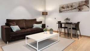 A modern living room with a brown sofa, a white coffee table, and a dining area with a table and chairs. - One-bedroom apartment with street views (Barcelona)