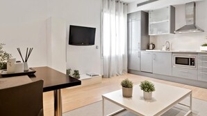 A modern kitchen with stainless steel appliances, a flat-screen TV mounted on the wall, and a dining area with a table and chairs. - One-bedroom apartment with street views (Barcelona)