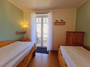 A room with two wooden beds, a wooden dresser, a small table with a lamp, and a balcony with chairs.