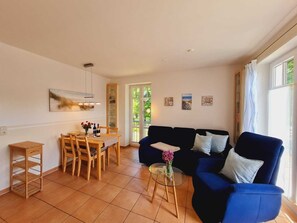 A living room with a blue sofa, a dining table with chairs, and a small glass table with a vase.