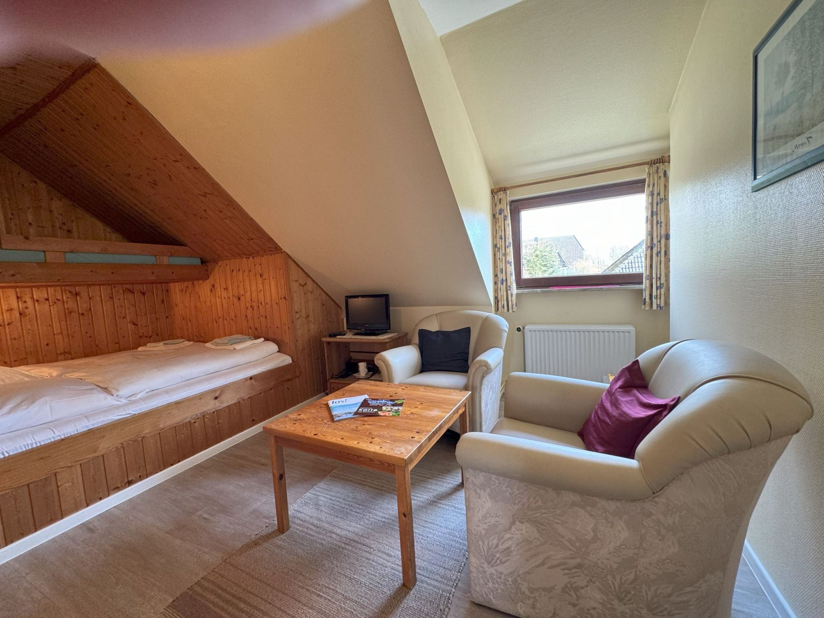 A cozy room with a wooden bunk bed, a small table with a magazine, a TV, a chair, and a sofa.