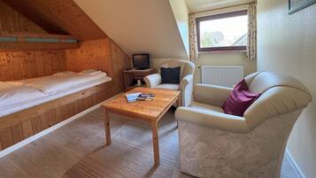 A cozy room with a wooden bunk bed, a small table with a magazine, a TV, a chair, and a sofa.