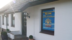 A building with a white exterior, a blue sign advertising 'big sun studio solarium', and potted plants on the ground. - Reiterhof Wollesen (Süderlügum)