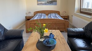 A bedroom with a wooden bed, a painting on the wall, a table with a vase of flowers, and a window with blinds. - Reiterhof Wollesen (Süderlügum)