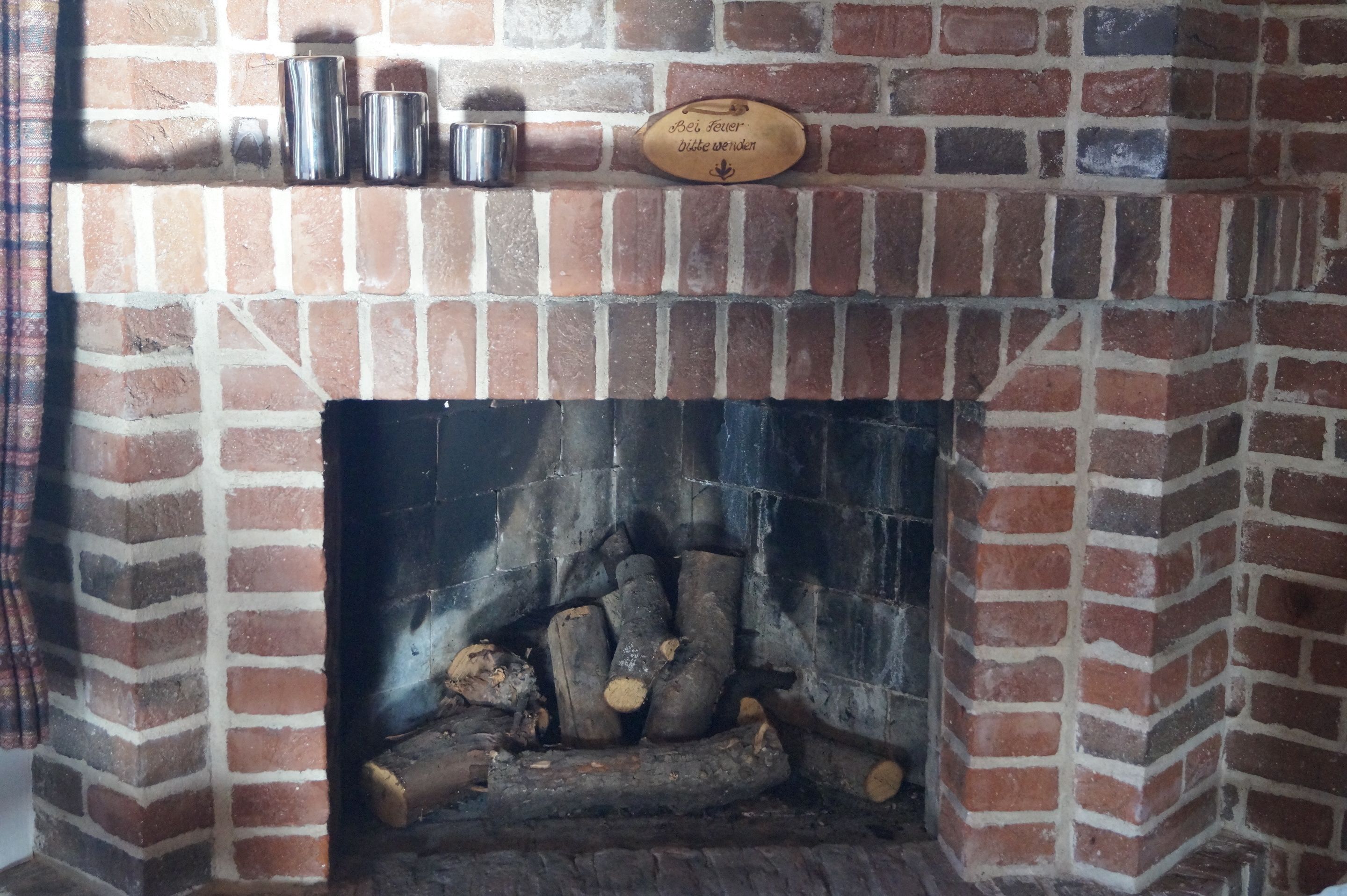 A brick fireplace with a plaque, metal containers, and logs.