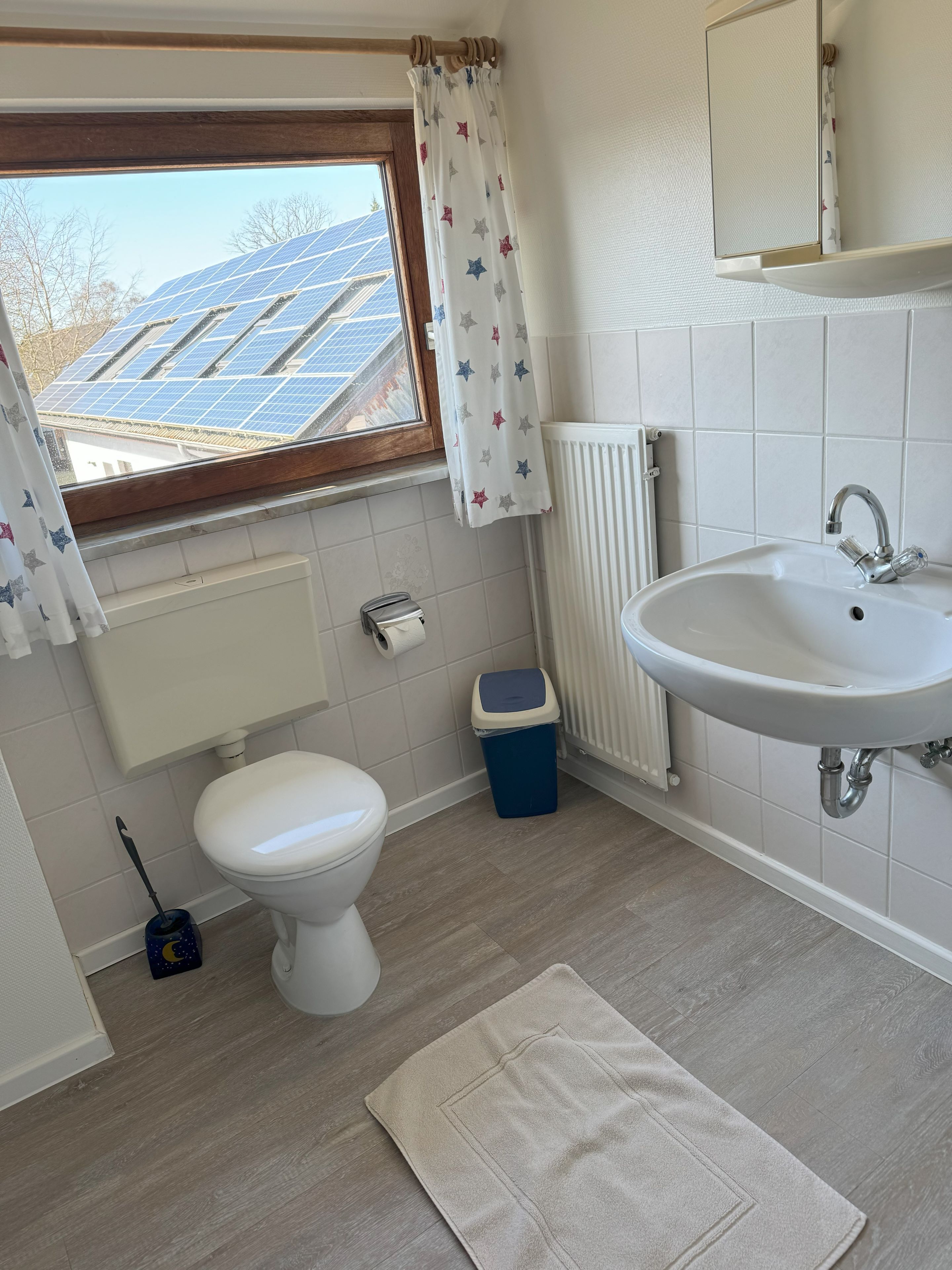 A bathroom with a toilet, sink, and window with solar panels outside.