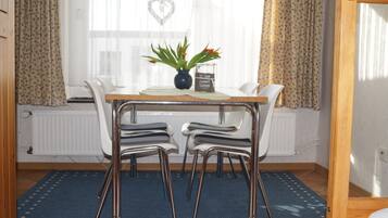 Un comedor con una mesa de madera, dos sillas blancas, un tapete azul y un jarrón con flores.