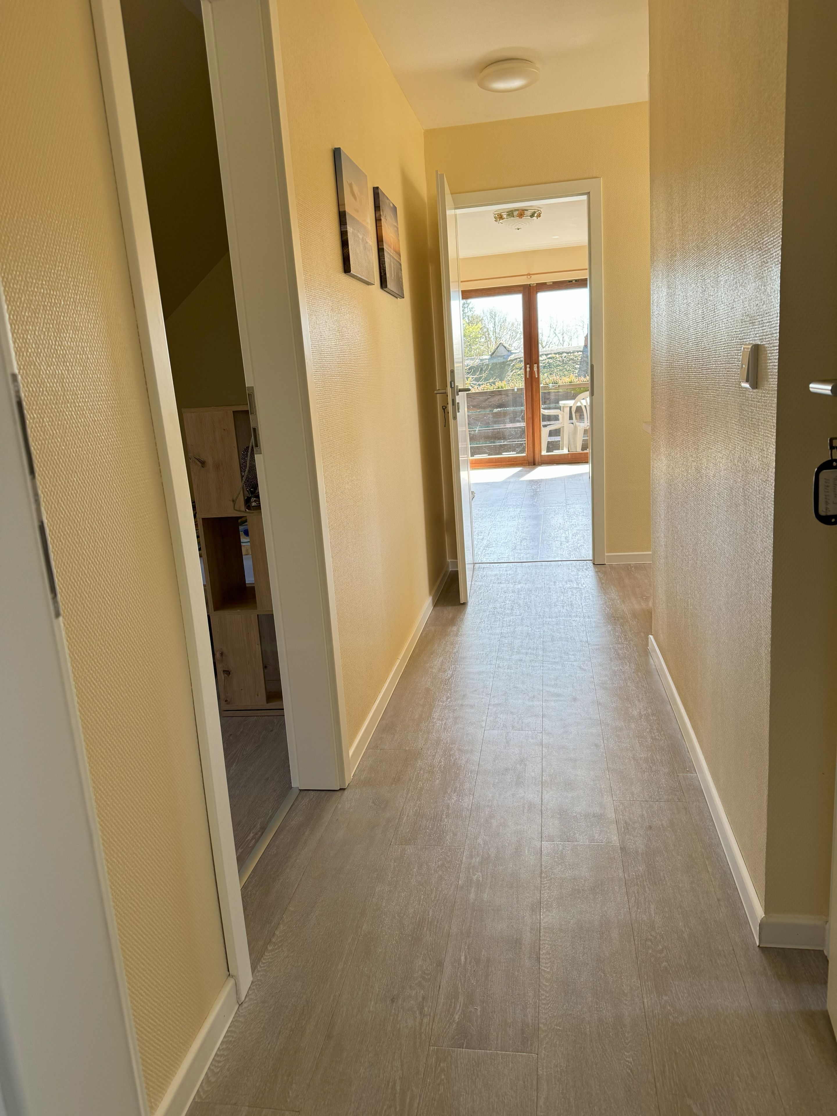 Un pasillo con paredes color beige y piso de madera, que conduce a una puerta con vista a un patio trasero.