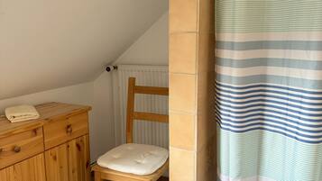 Een kleine, knusse kamer met een houten kast, een comfortabele stoel en een kamerbadgordijn met strepen.