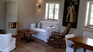 A cozy living room with a white sofa, a wooden rocking chair, a small table, and a fireplace. - Stylish vacation in one of the most beautiful areas of Germany (Ankershagen OT Rumpshagen)