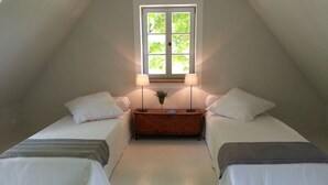 A small, cozy attic bedroom with two single beds, a nightstand, and a window with a view of greenery. - Stylish vacation in one of the most beautiful areas of Germany (Ankershagen OT Rumpshagen)