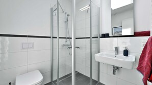 Un baño moderno con ducha de vidrio, un lavamanos blanco y un inodoro.