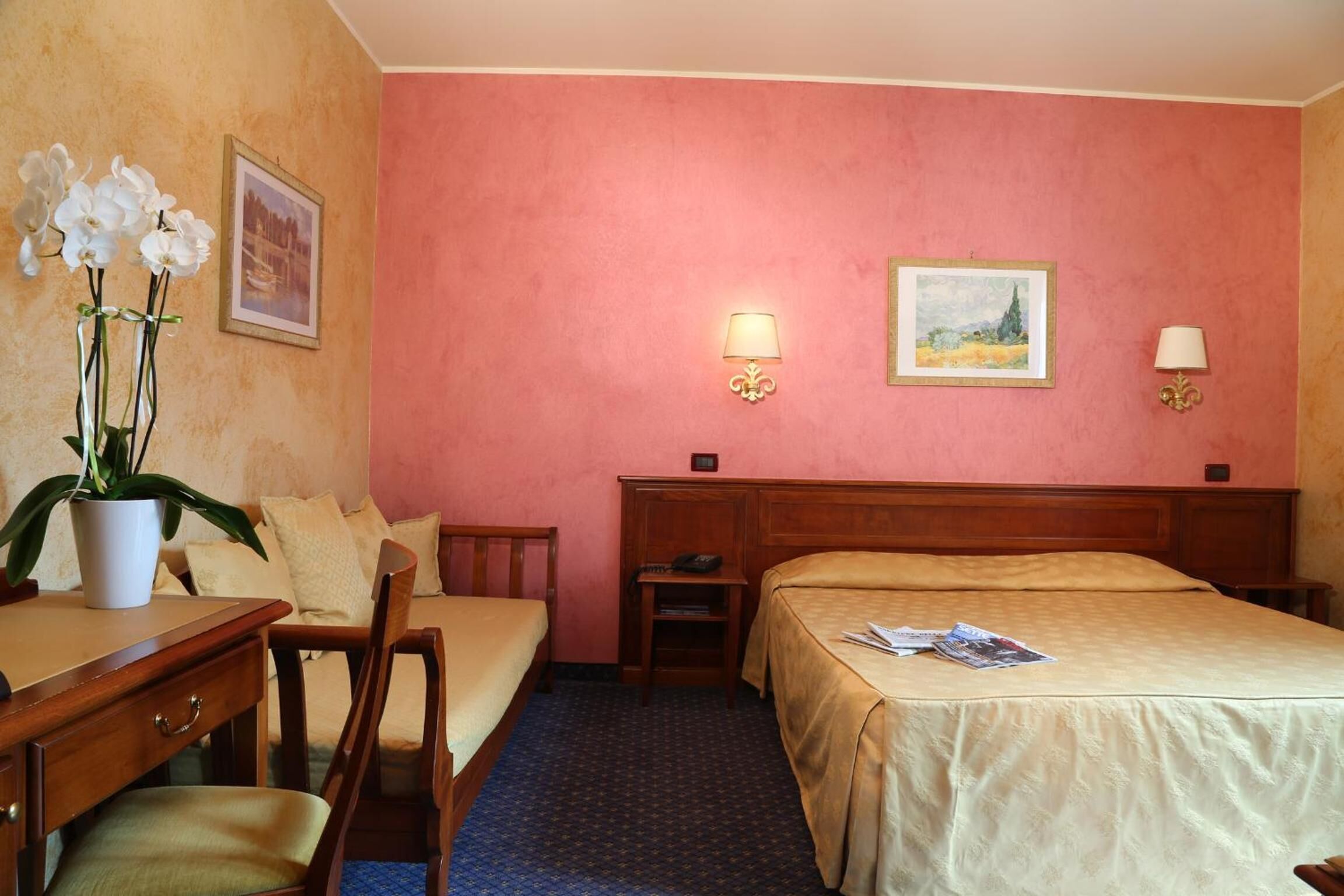 Habitación de hotel con una cama, un escritorio con silla, una mesita y una planta en maceta.