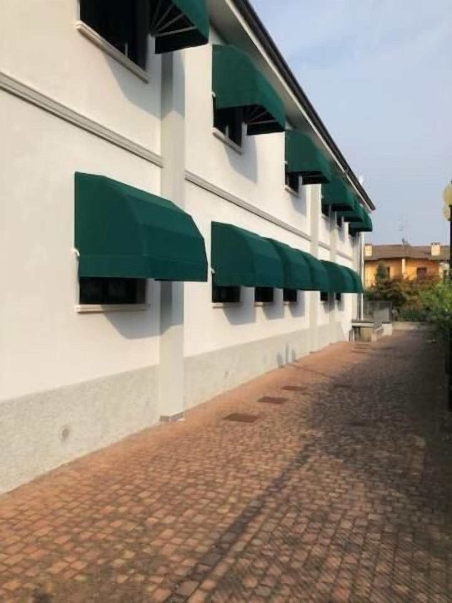 Ein Gebäude mit weißer Fassade und grünen Markisen über den Fenstern.