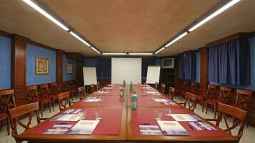 Une salle de conférence équipée de longues tables, de chaises, d’un tableau blanc et d’un écran de projection.