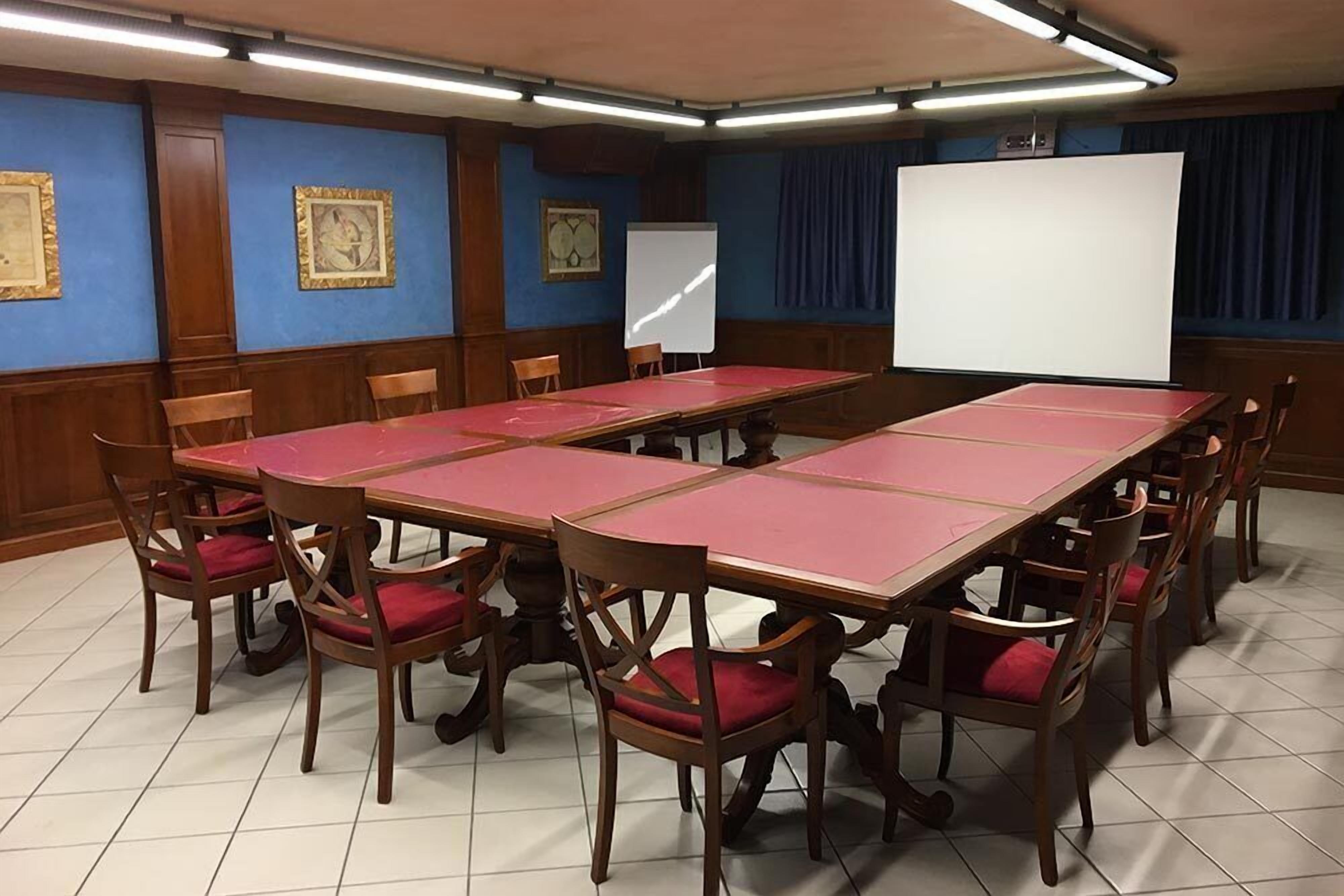 Ein Konferenzraum mit langem Tisch und Stühlen, einer Whiteboard und gerahmten Bildern an den Wänden.