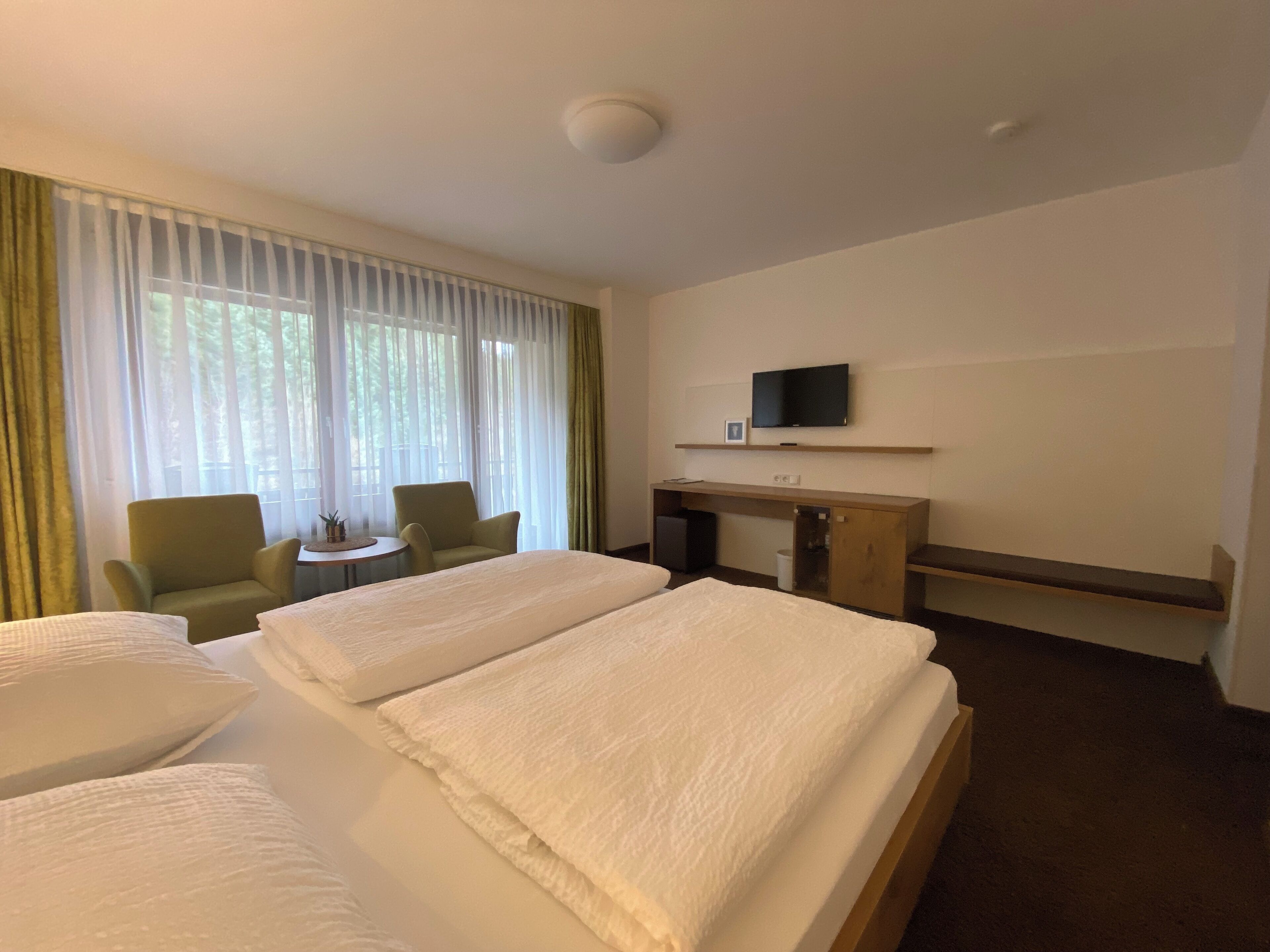A hotel room with two beds, a desk, a chair, a television, and a window with curtains.