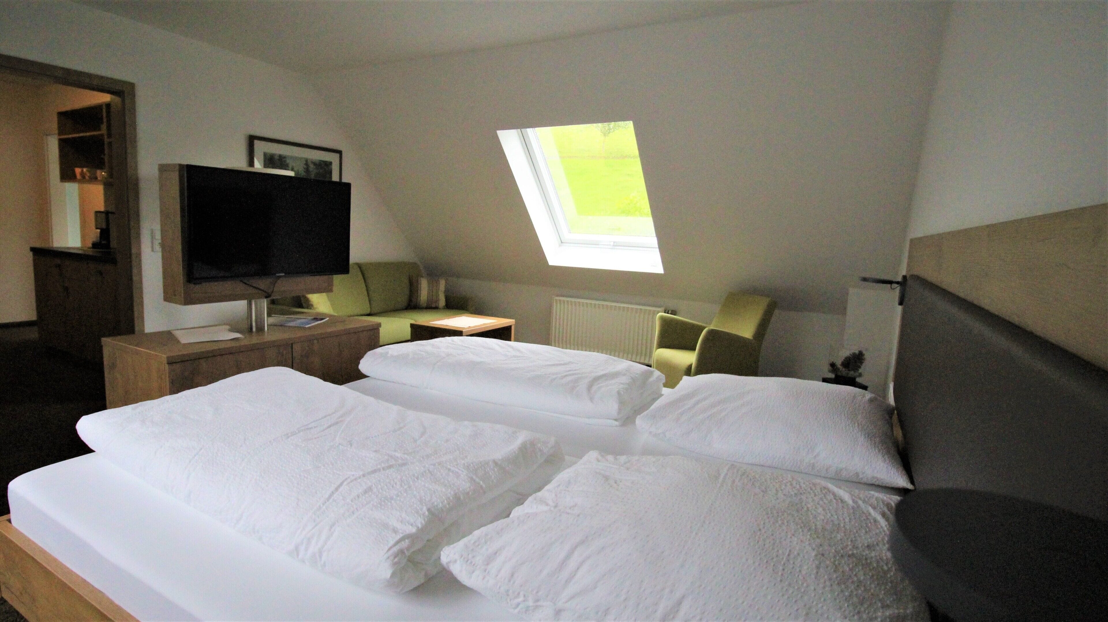 Une chambre d’hôtel avec un grand lit, un téléviseur posé sur un meuble en bois, un bureau avec une chaise et une fenêtre donnant sur un paysage verdoyant.