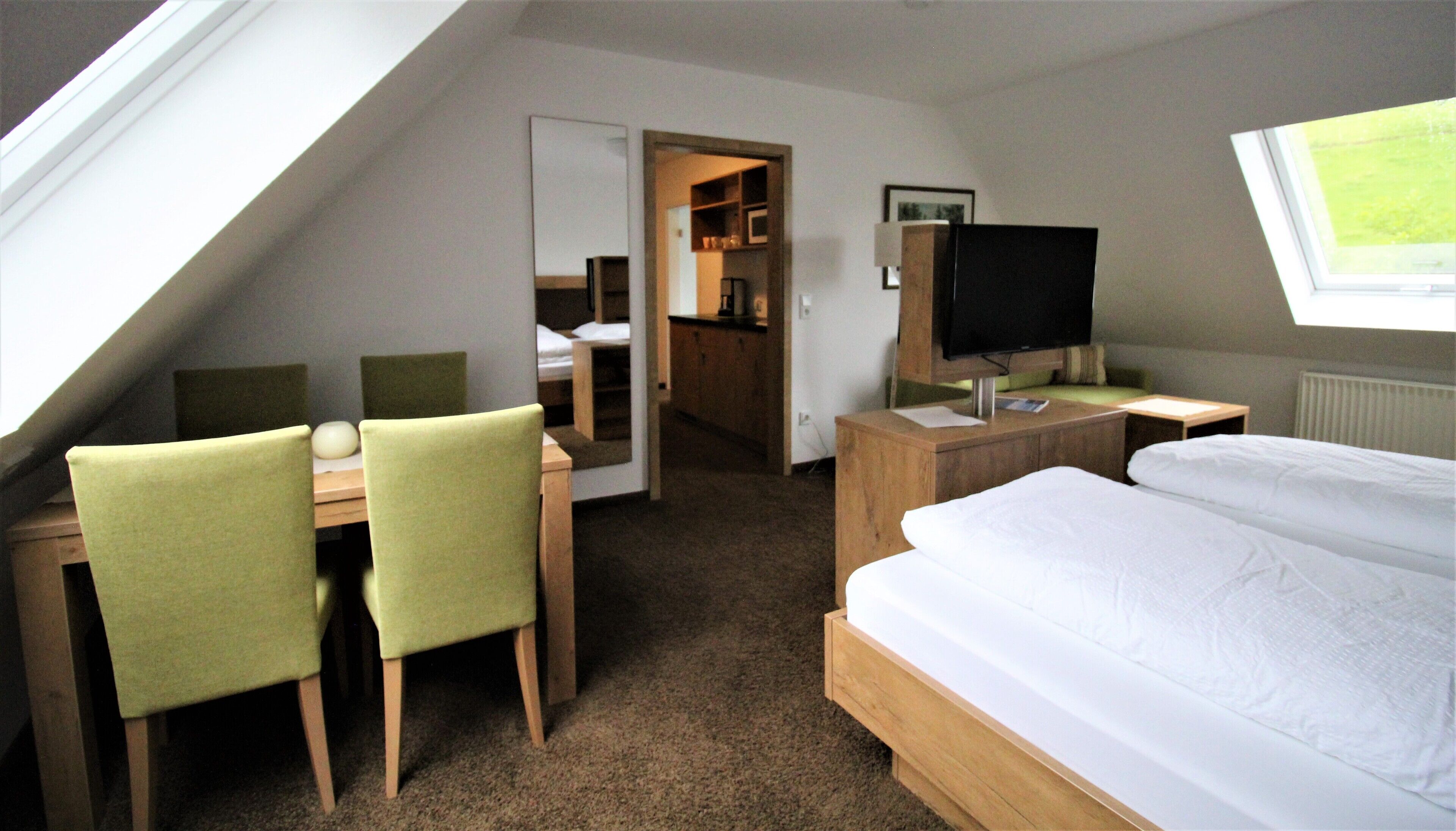 Habitación de hotel con cama, escritorio con dos sillas, televisión y baño visible a través de una puerta abierta.