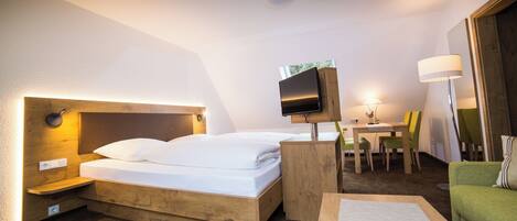 Habitación de hotel con una cama de madera, un escritorio con silla, un televisor en la pared y una lámpara sobre el escritorio.