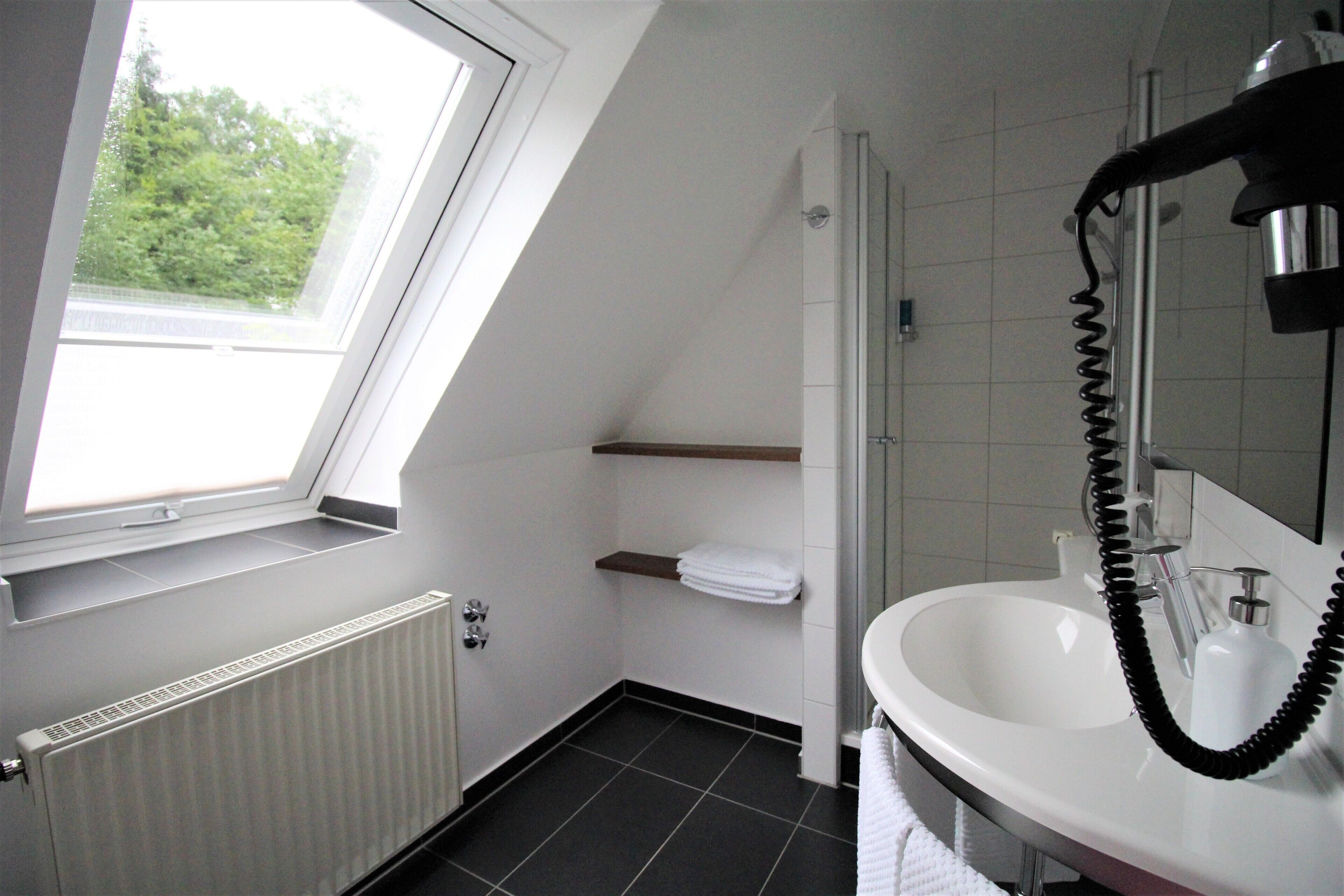 A bathroom with a skylight, a white sink, a towel rack, and a shower.