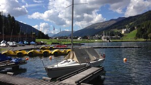 Una marina con una barca a vela ormeggiata a un molo di legno, immersa in acque calme e con un paesaggio montuoso sullo sfondo.