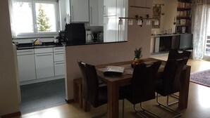 Una cucina moderna con mobili bianchi, un tavolo da pranzo con sedie e una televisione nella zona soggiorno.