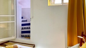 Una habitación con una cama, una ventana con cortinas amarillas, un ventanal con vistas a un paisaje nevado y una estantería con adornos.