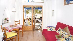Una habitación con sofá rojo, sillas de madera, una mesa de comedor con mantel blanco y un ventanal con vistas al exterior.