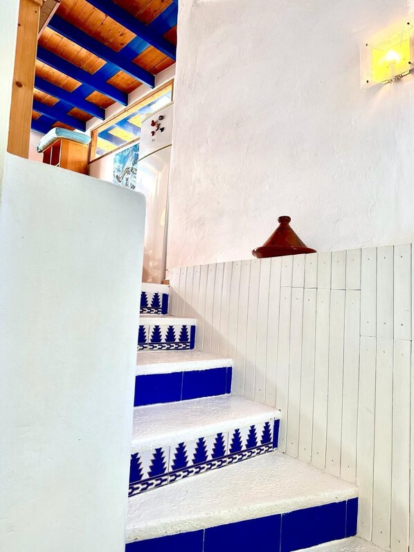 Eine Treppe mit weißen Wänden und blauen Stufen, die zu einer Holzbalkendecke führt.