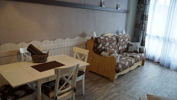A cozy room with a wooden sofa, a dining table, and chairs.
