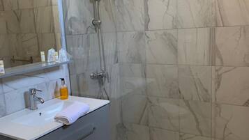 A modern bathroom with a glass shower enclosure, a white sink with a mirror, and a marble-tiled shower wall.
