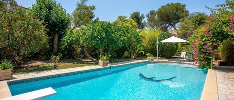 A clear blue swimming pool surrounded by lush greenery and trees.