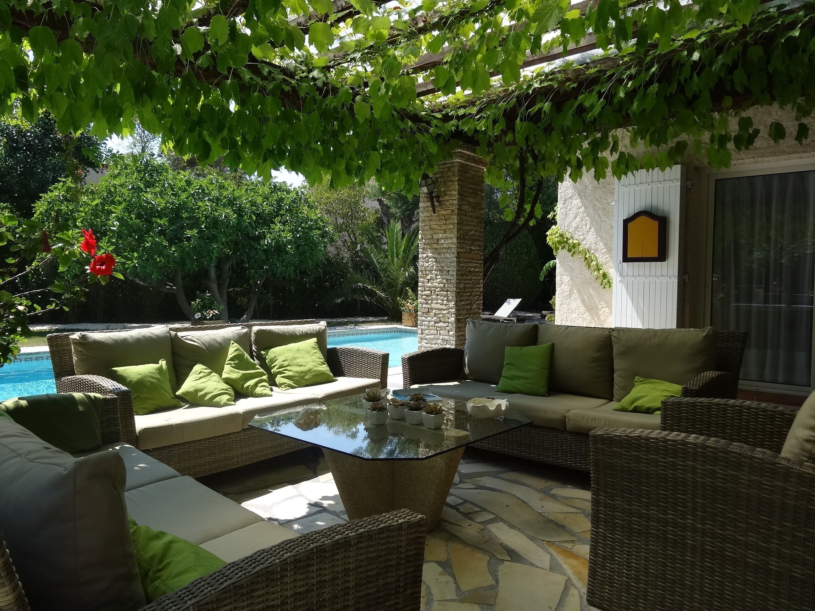 Une terrasse extérieure avec des meubles en osier, une table basse en verre et un sol en pierre.