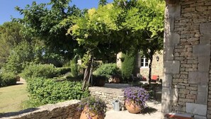 An outdoor seating area with stone walls, potted plants, and a view of a garden and building in the background. - Mas des Papillons, Gordes (Gordes)