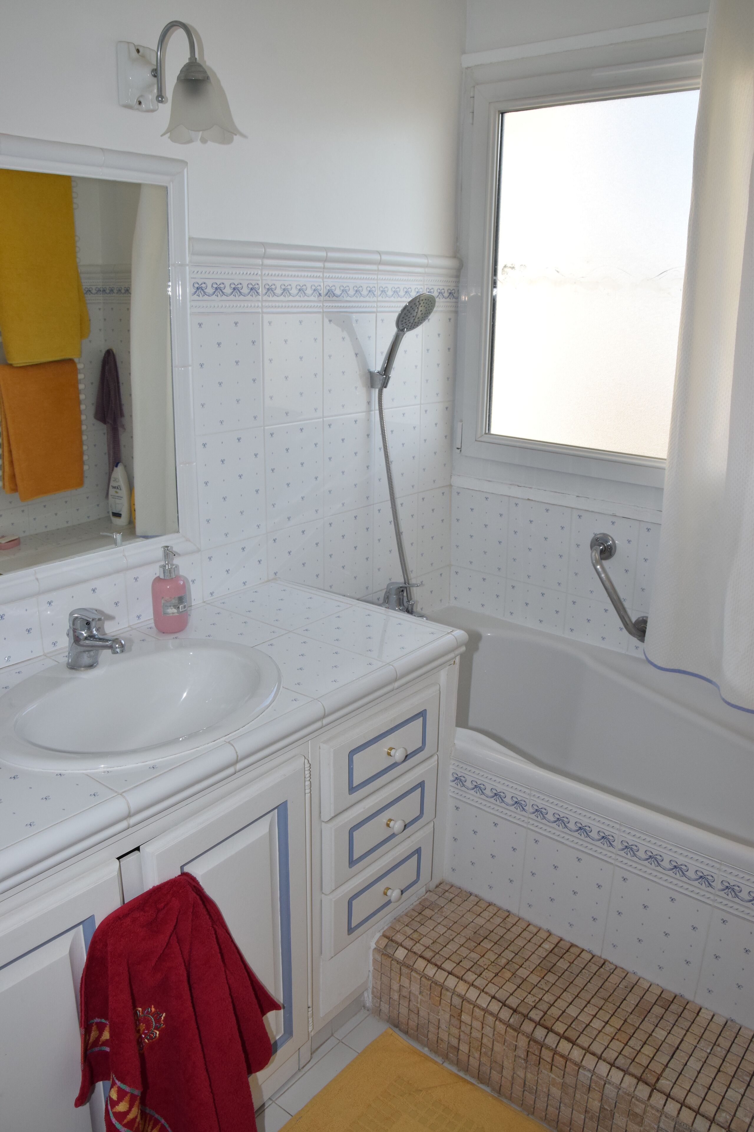 A bathroom with a white sink, mirror, and a shower with a window.