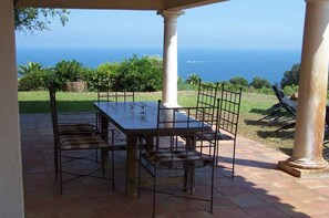 An outdoor patio with a table and chairs, a view of the ocean, and a stone pathway.