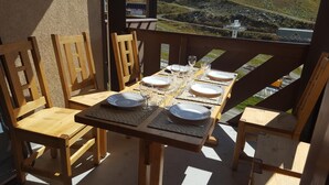 A wooden dining table set for four with chairs, a view of a mountainous landscape, and a building in the background. - 3-room apartment, ski-in/ski-out, adjacent to ski slopes and lifts, sleeps 4/6 (Val Thorens)