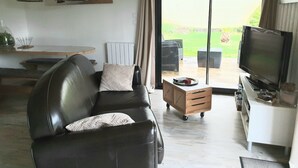 Un salon moderne avec un canapé en cuir, un téléviseur et une porte-fenêtre coulissante donnant sur une terrasse extérieure.
