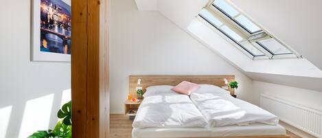A bedroom with a skylight, a bed, a nightstand, a plant, and a framed picture on the wall.