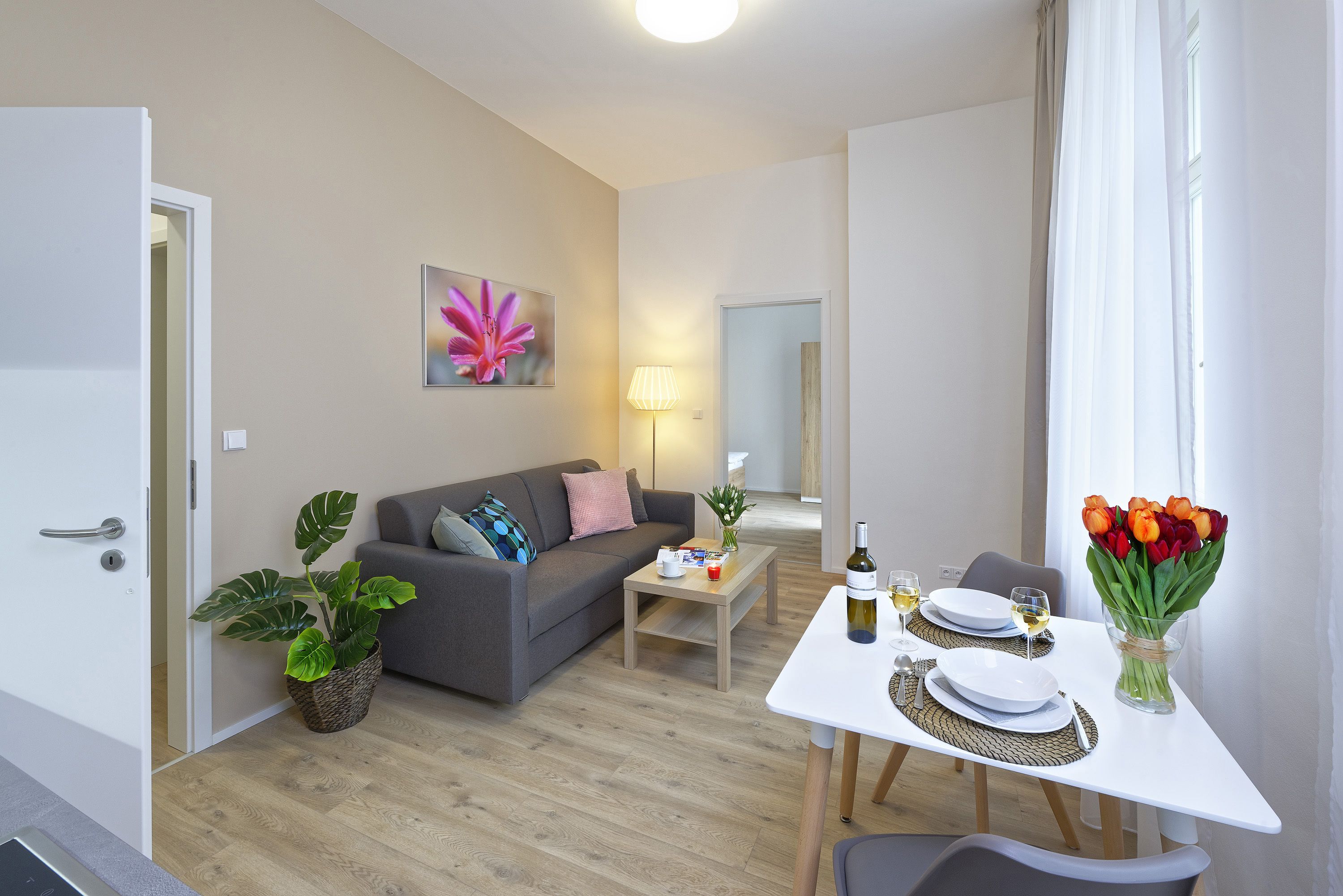 A modern living room with a grey sofa, a coffee table, and a dining table set for two.