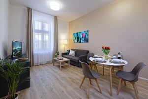 Una sala de estar moderna con sofá, mesa de centro, mesa de comedor y sillas. Hay un televisor sobre un mueble, una lámpara y un cuadro en la pared.