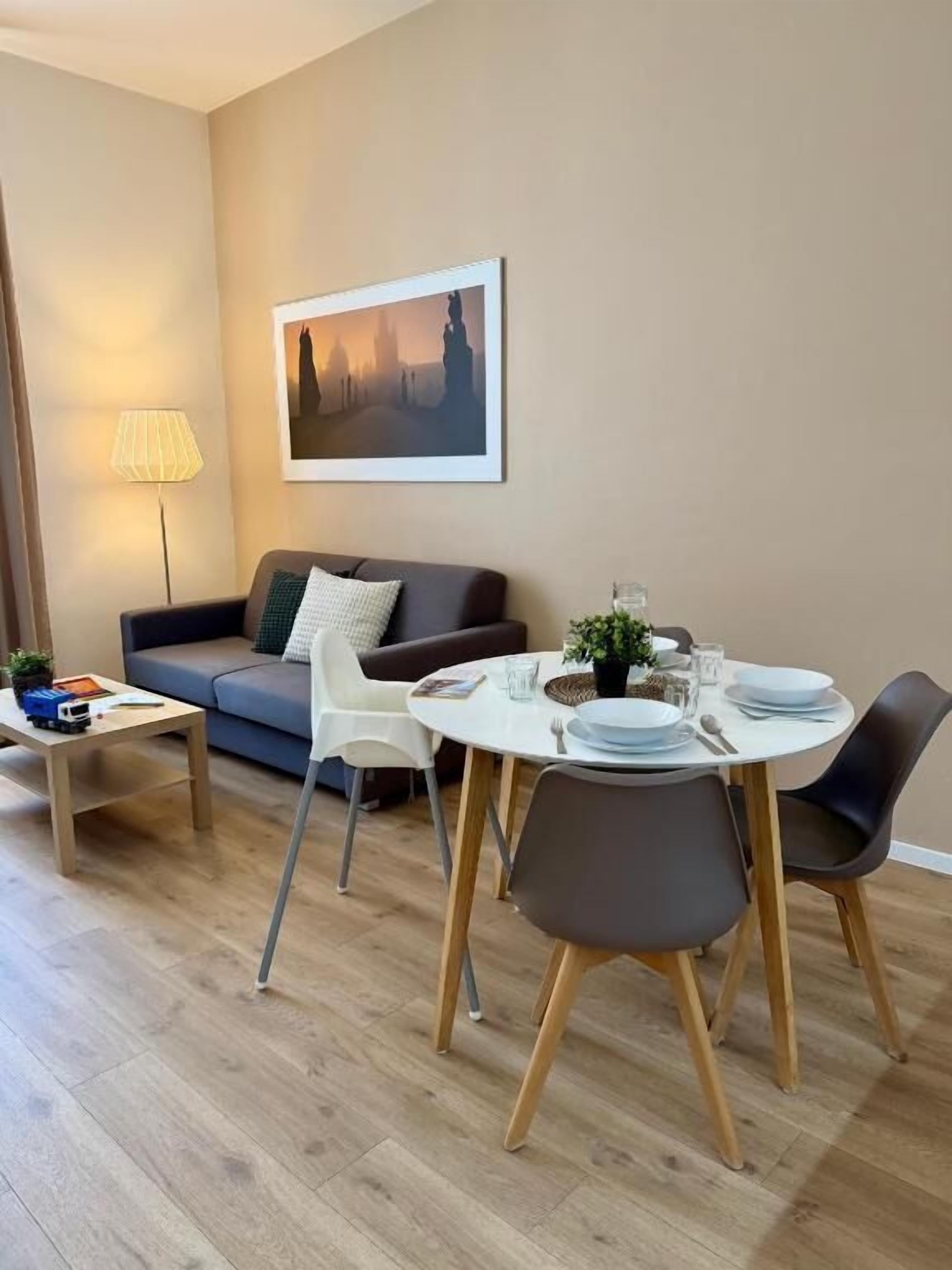 Una sala de estar moderna con sofá, mesa de comedor, sillas y una lámpara.