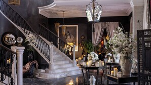A grand staircase with a marble finish, leading to a room with a chandelier, a large vase with white flowers, and a black and white patterned floor. - Palais Ronsard (Marrakech)
