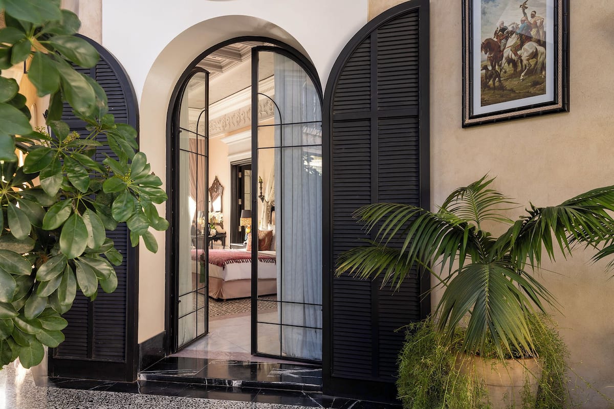A hotel entrance with a glass door, a framed painting, and potted plants.