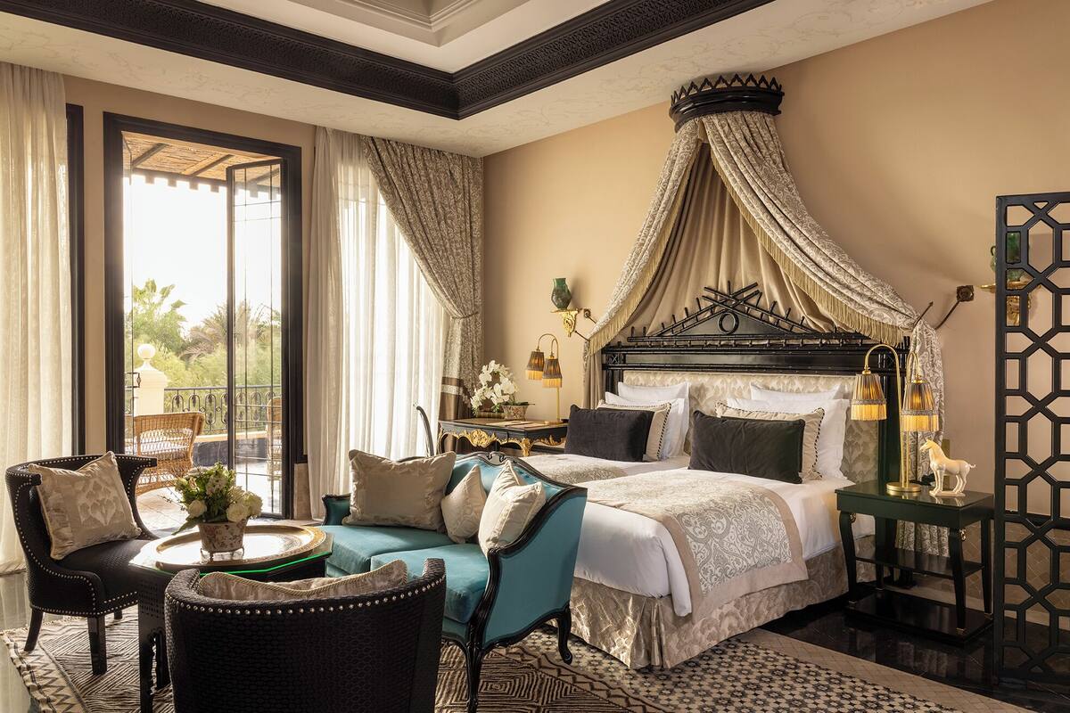 A spacious bedroom with a large bed, a sitting area with a chair and a small table, and a view of the outdoors through a large window.