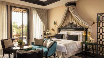 Une chambre spacieuse avec un grand lit, un coin salon comprenant un fauteuil et une petite table, et une vue sur l’extérieur grâce à une grande fenêtre.