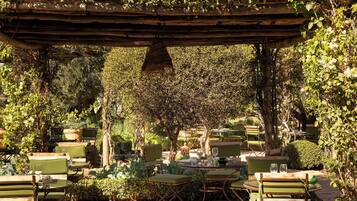 An outdoor patio area with tables and chairs, surrounded by lush greenery and trees.
